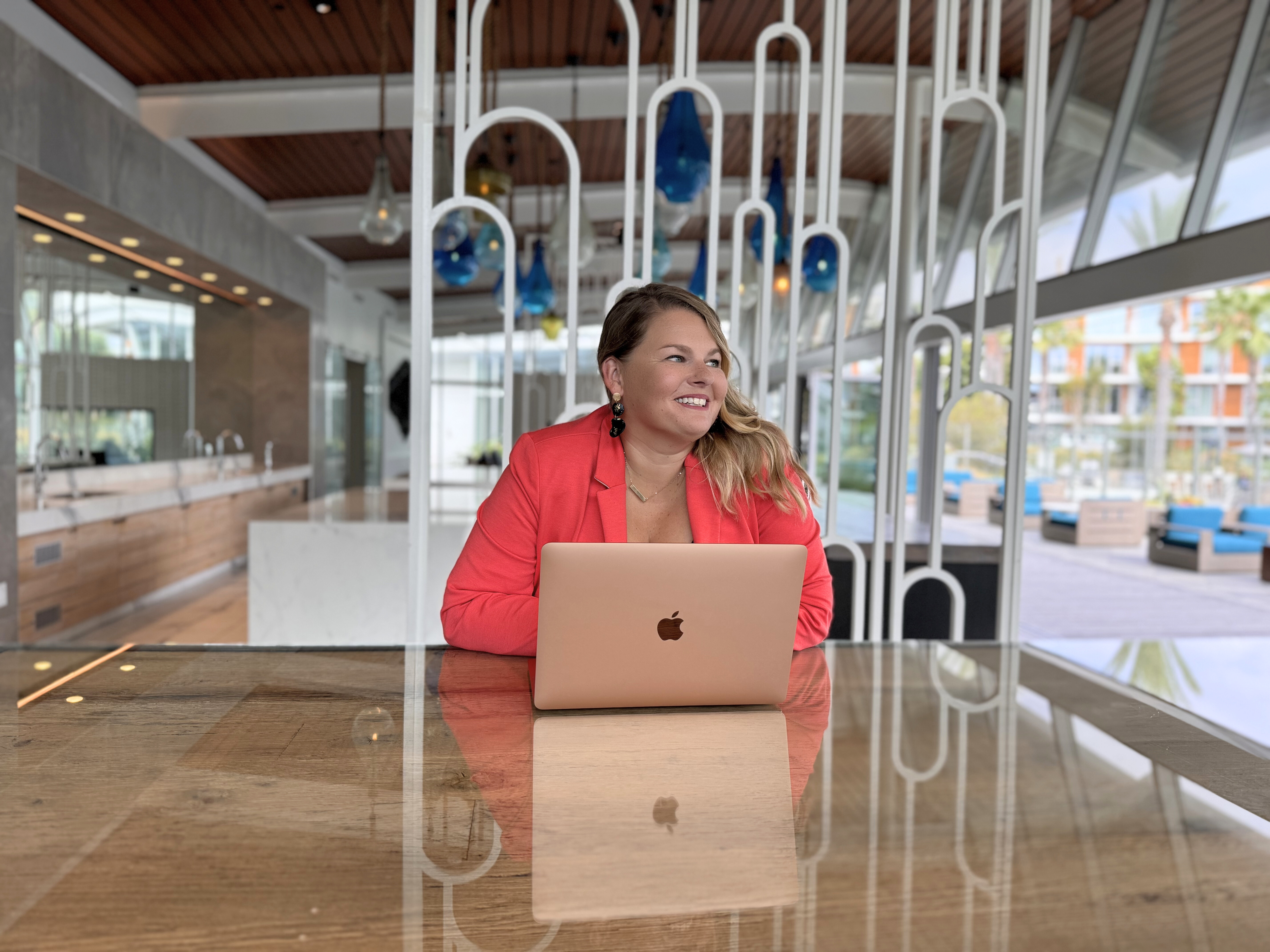Photo of Lynn Marie Debilzen, founder of The Collective Shift Co., smiling and looking into the distance, with a laptop. 