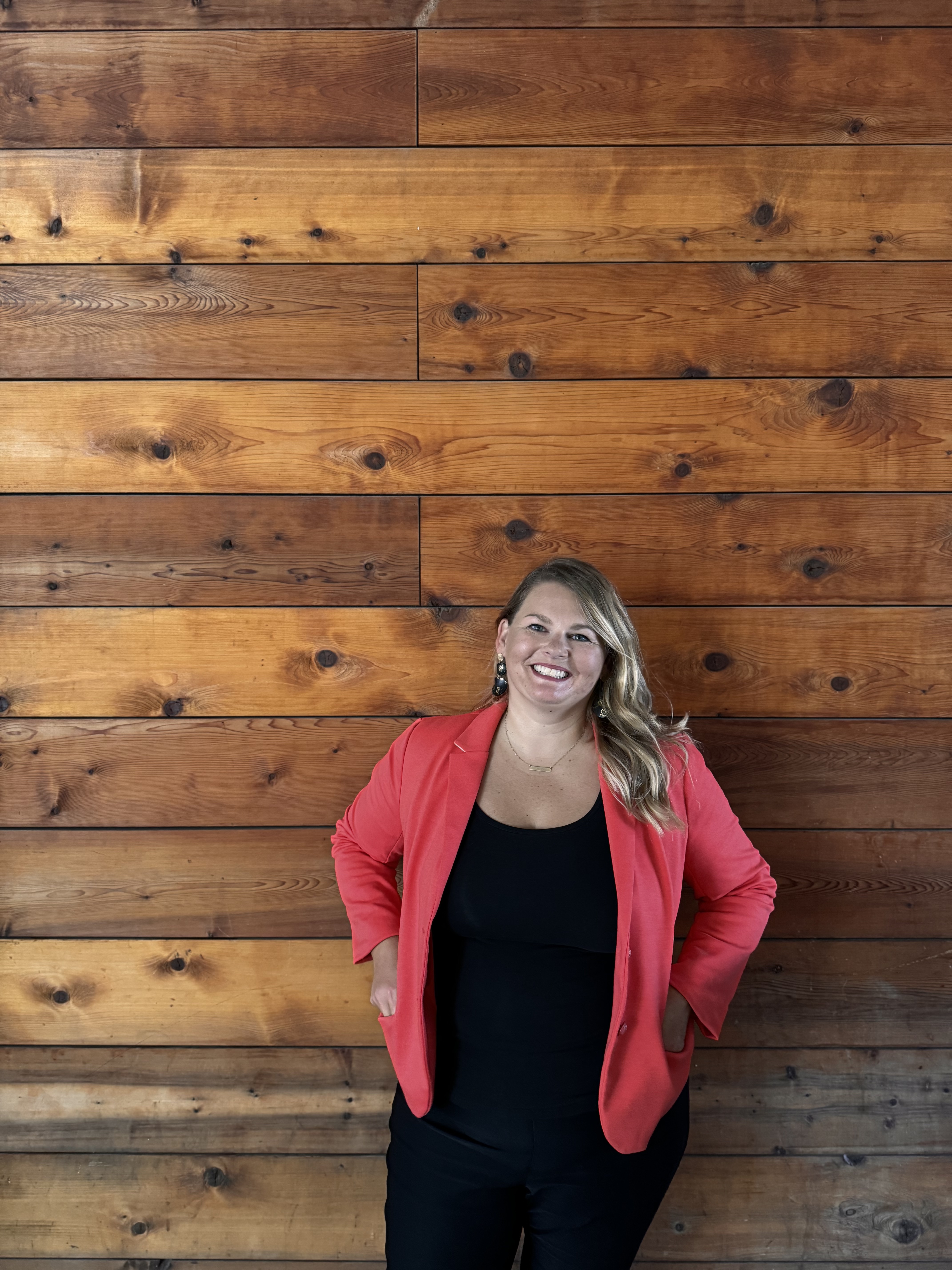 Photo of Lynn Marie Debilzen, founder of The Collective Shift Co., smiling and in front of a wooden wall